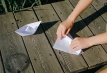 Jak zacząć origami modułowe w domu: poradnik dla dzieci i dorosłych Dłonie składają papierowe łódki na drewnianym blacie