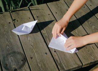 Jak zacząć origami modułowe w domu: poradnik dla dzieci i dorosłych Dłonie składają papierowe łódki na drewnianym blacie