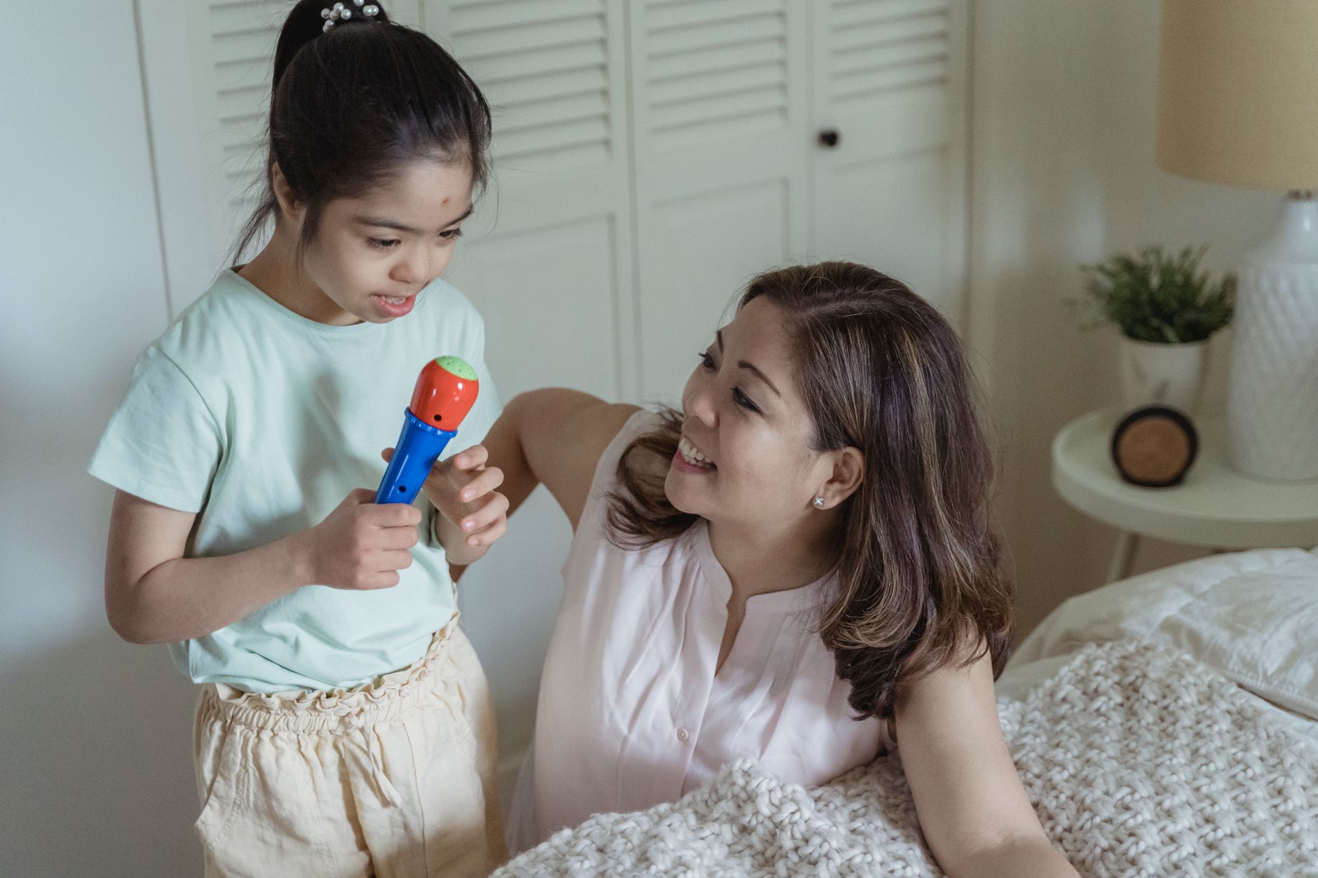 Uśmiechnięta mama bawi się z córką trzymającą zabawkowy mikrofon